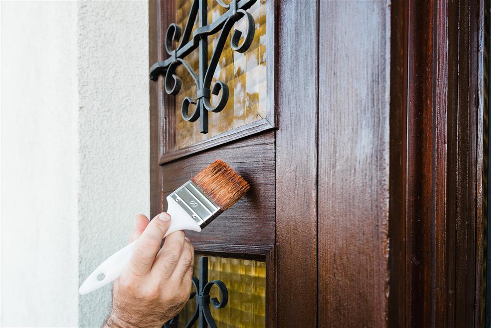 Photo of someone staining or sealing a door with a large natural hair paint brush.